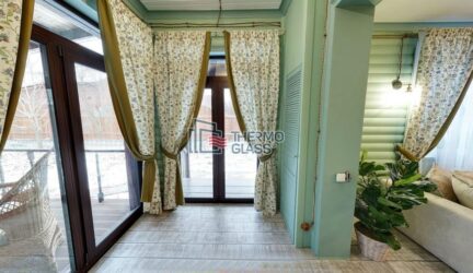 Стеклянные окна до пола в коричневой раме украшают выход на веранду